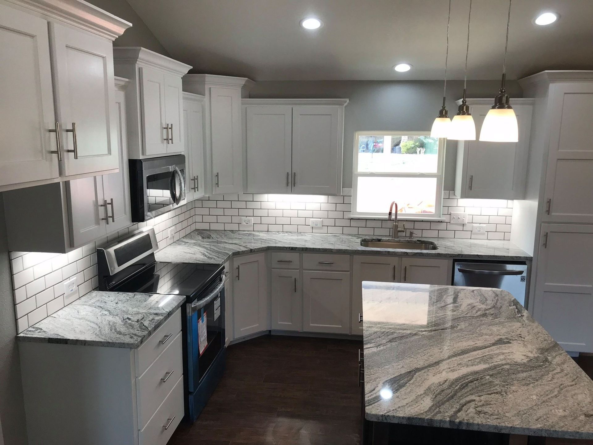 White kitchen with granite countertops, stainless steel appliances, and island with pendant lights.