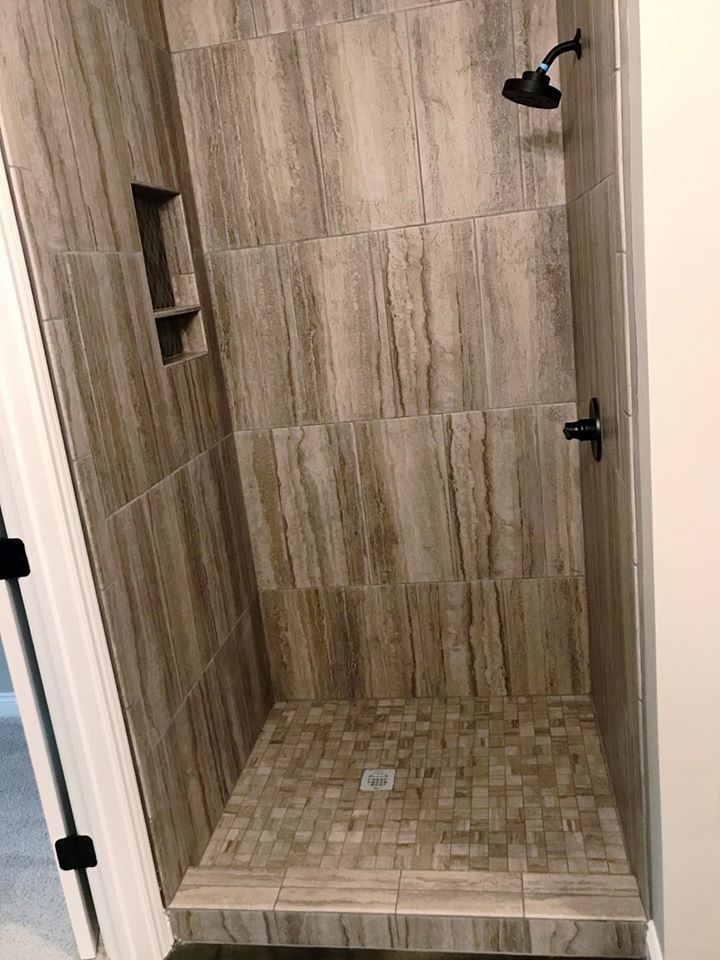 Tiled shower with dark fixtures and built-in shelf. Brown mosaic floor and wood-look wall tiles.