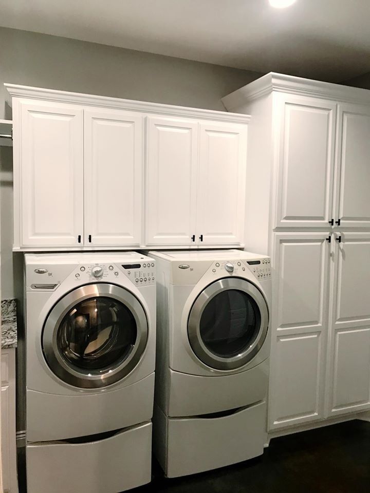 Laundry room with a white washer and dryer, white cabinets above and to the right. Dark floor.