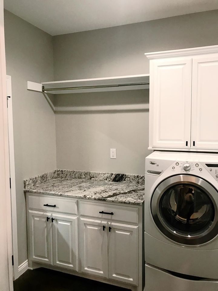 Laundry room with white cabinets, granite countertop, washer, dryer, and hanging rod.