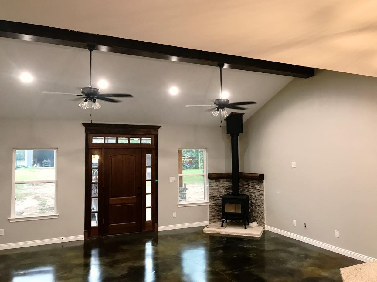 Interior living space with wood door, stone fireplace, two ceiling fans, and concrete floor.