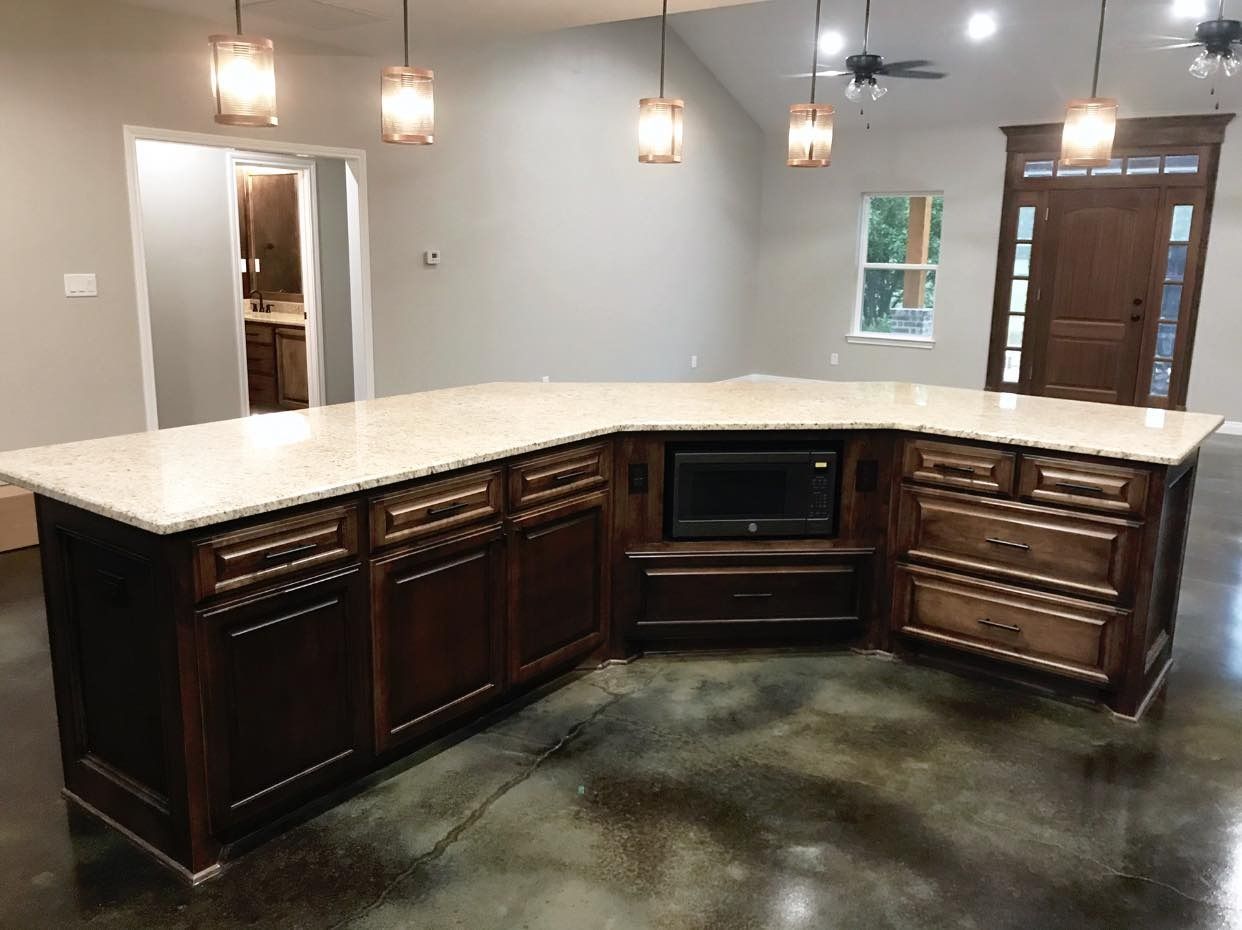 Dark wood kitchen island with beige countertop and built-in microwave, set in a spacious room with concrete floor.