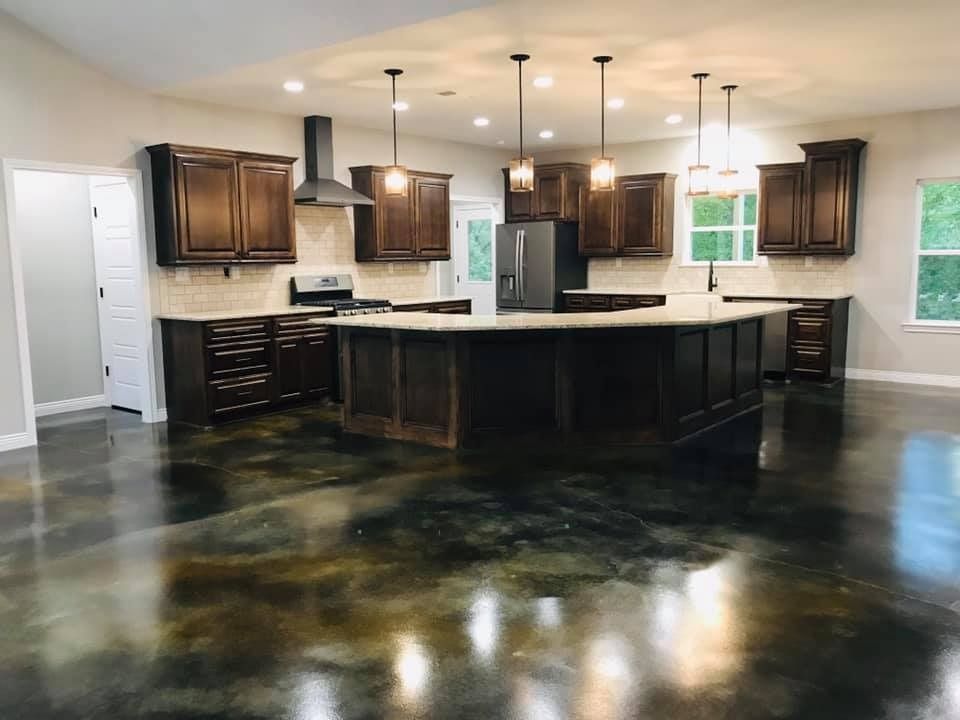Spacious kitchen with dark cabinets, a large island, stainless steel appliances, and a glossy, stained concrete floor.