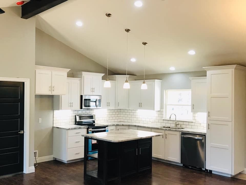 Modern white kitchen with black island, stainless steel appliances, and dark wooden floors.