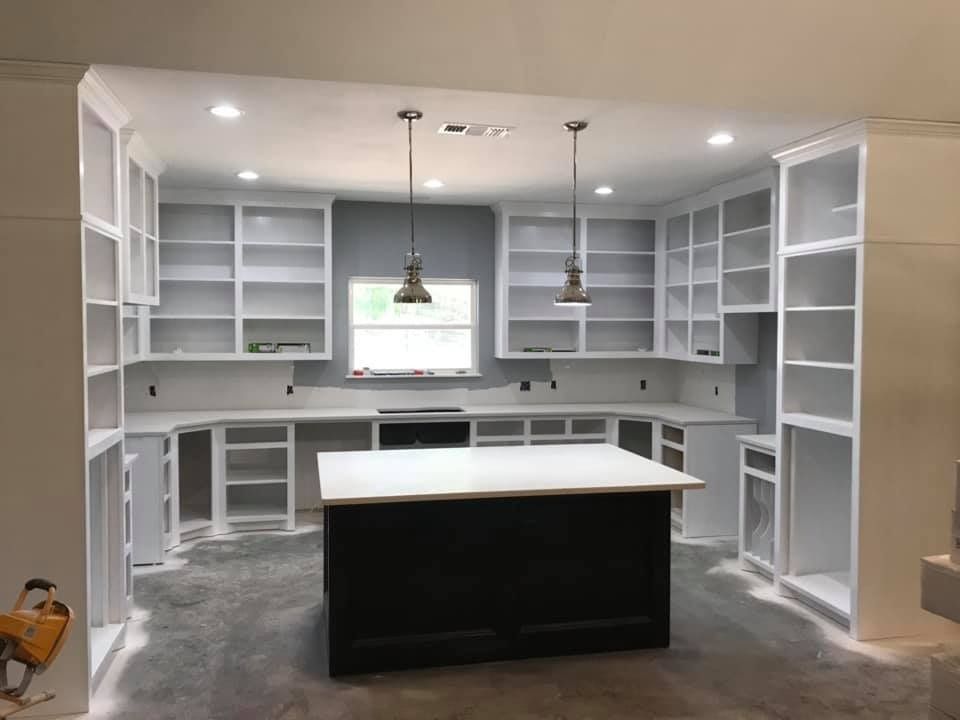 Kitchen renovation with white cabinets, dark island, and pendant lights.
