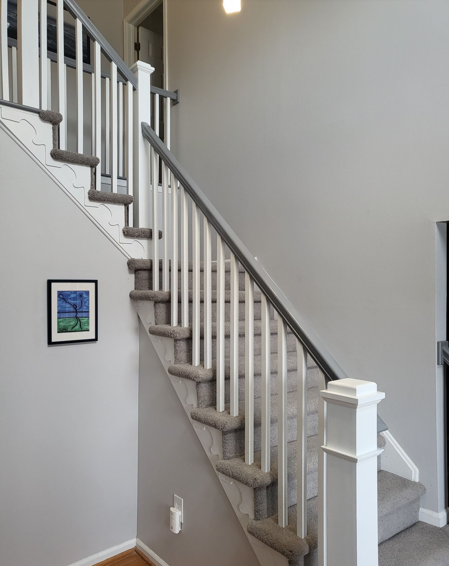 A staircase with a white railing and a picture on the wall.