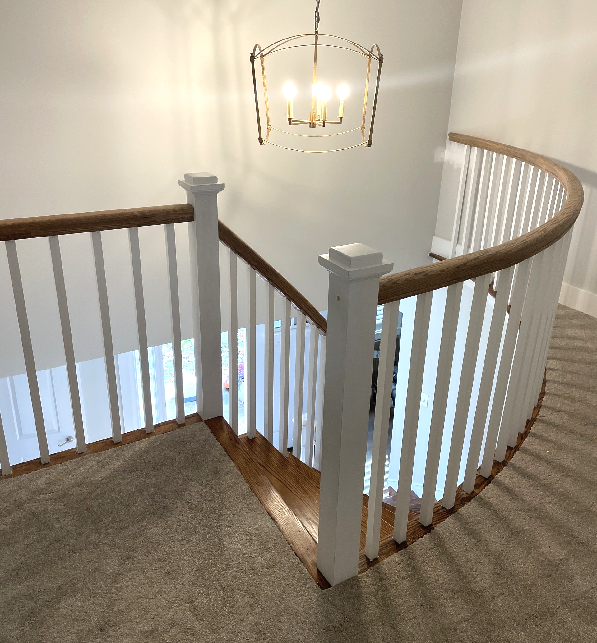 A curved staircase with a white railing and a chandelier hanging from the ceiling.