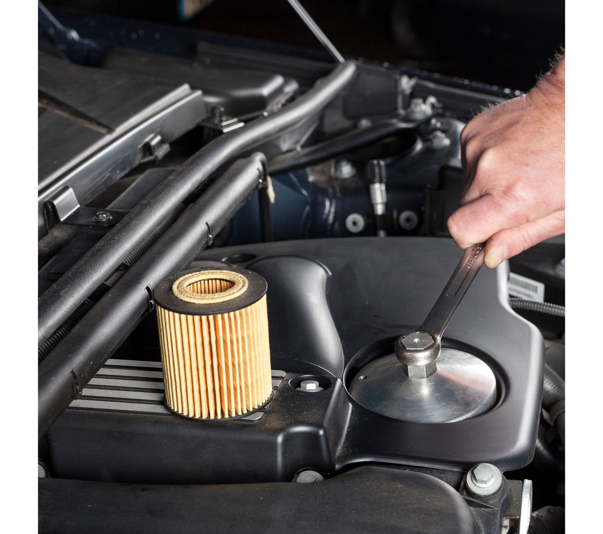 Mechanic's hand using a wrench to remove an oil filter on a car engine.