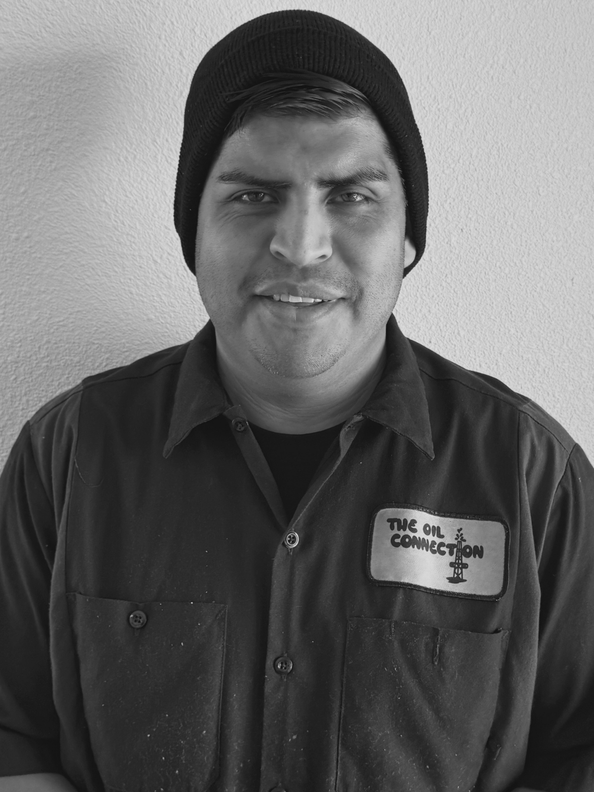 Man in black beanie and work shirt with "The Oil Connection" patch smiles.