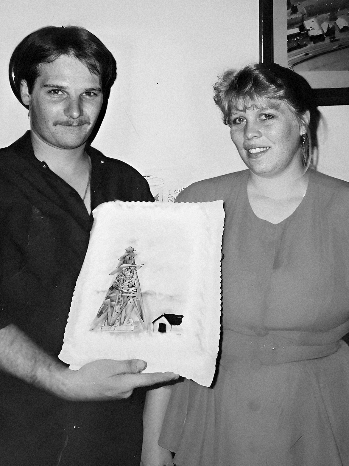 Man and woman holding a drawing of a snow-covered scene, smiling at the camera.
