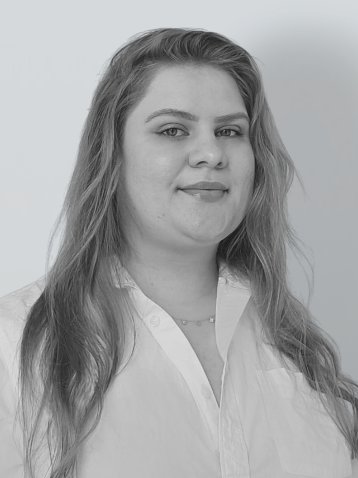 Woman with long hair, smiling, wearing a white collared shirt, looking directly at the camera.