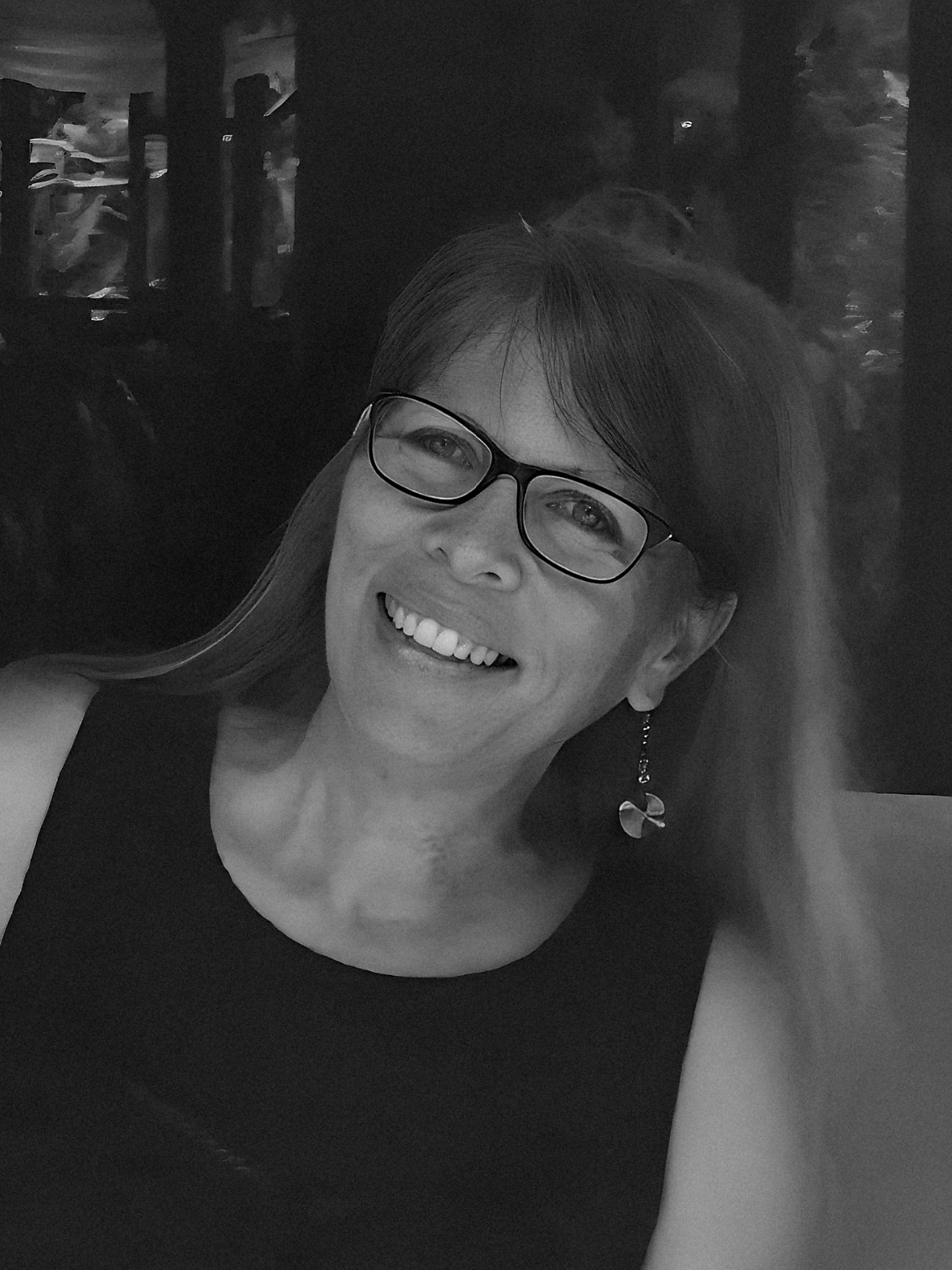 Woman with glasses smiles, wearing a sleeveless black top.