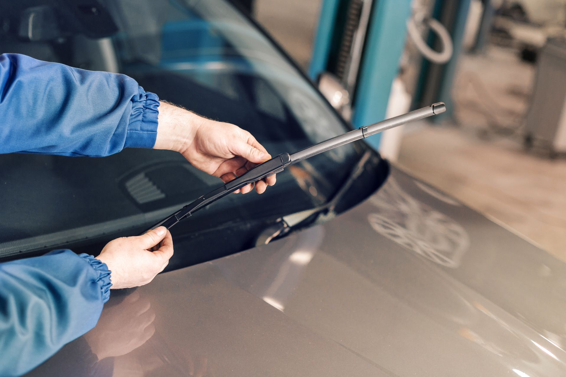 Hands replacing a windshield wiper on a gray car in a garage.