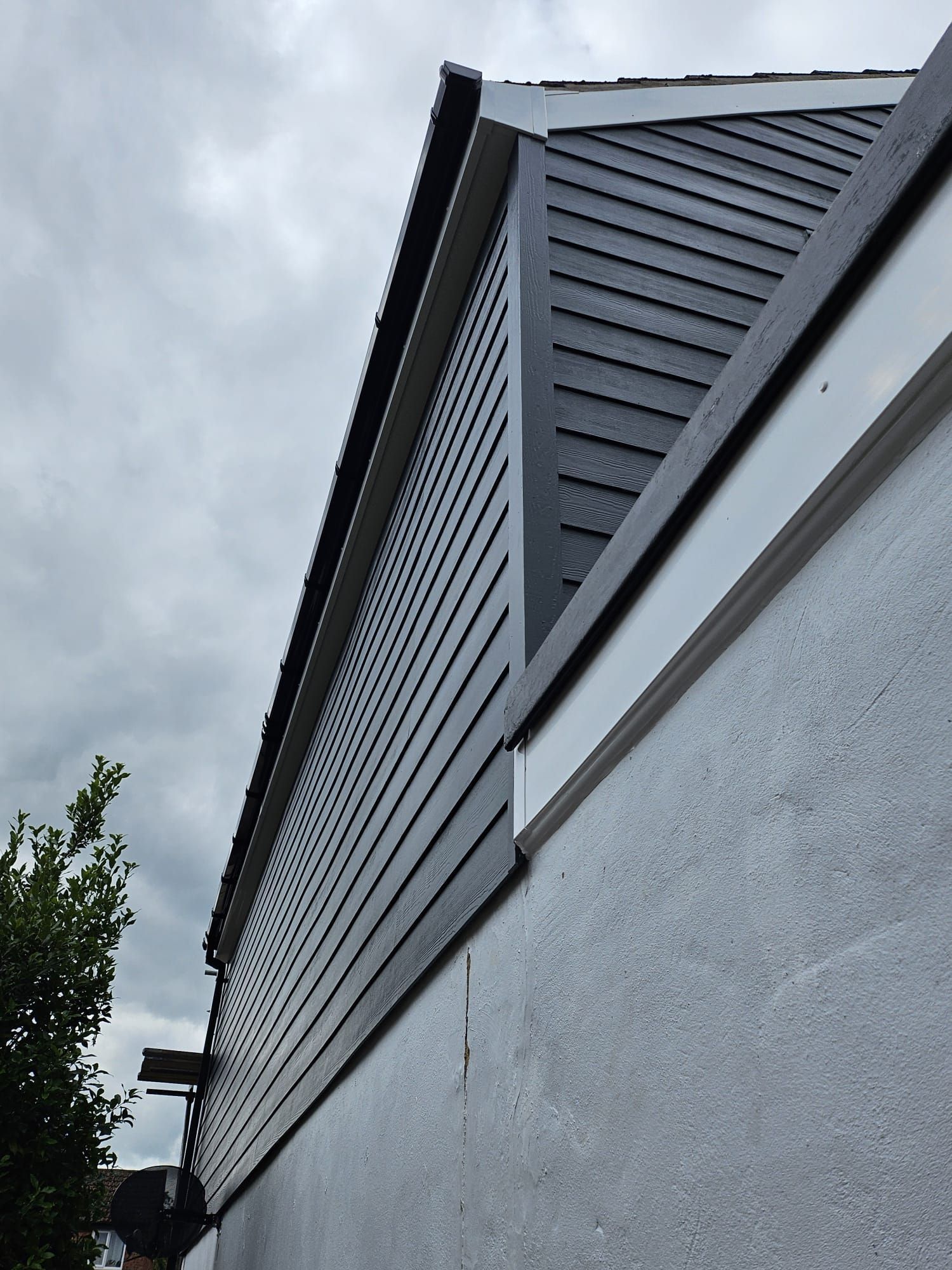 Low-angle view of the side of a building featuring dark gray horizontal siding above a light gray stucco wall.