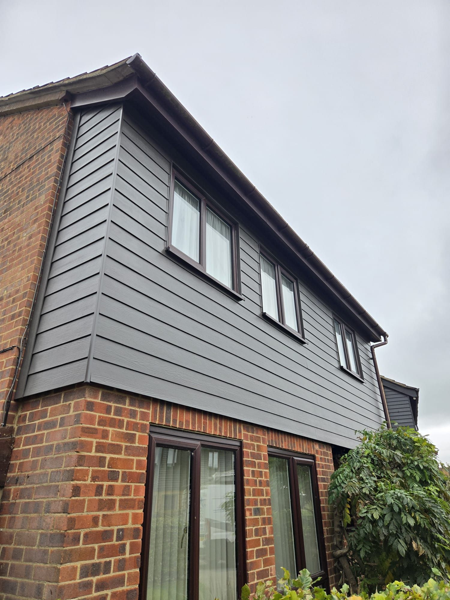 Exterior of a house with gray siding, brick, and brown trim on an overcast day.