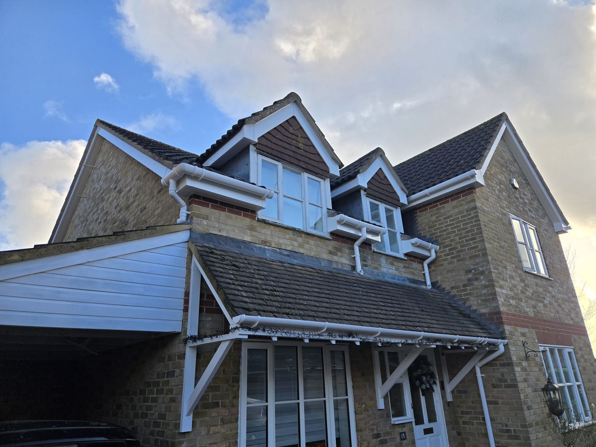 Two-story brick house with multiple gabled rooflines, white trim, and dormer windows under a cloudy sky.