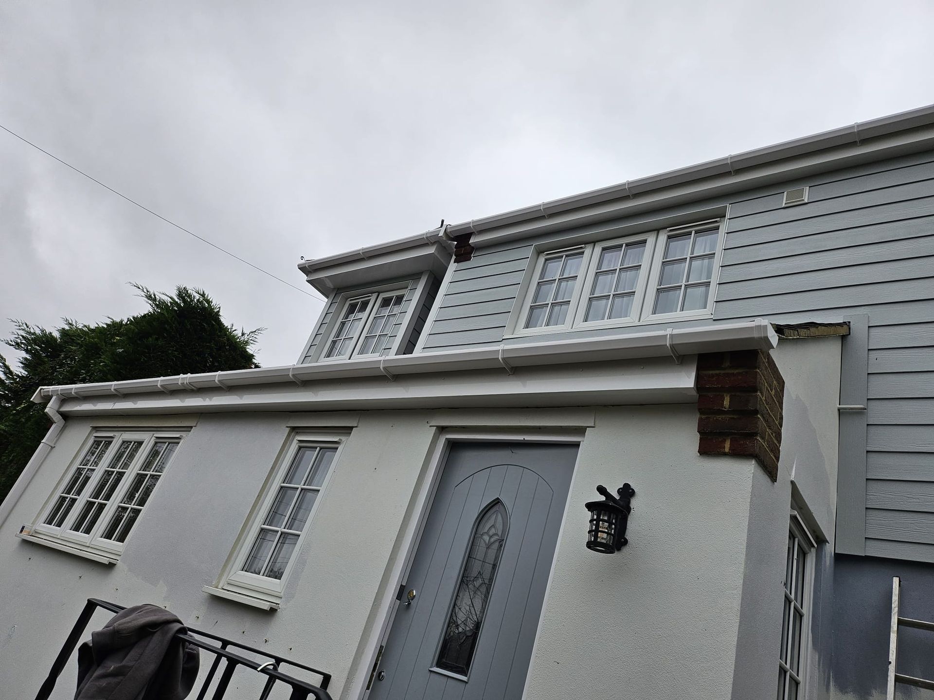Two-story house with gray siding and windows, white trim, and a gray door. Overcast sky.