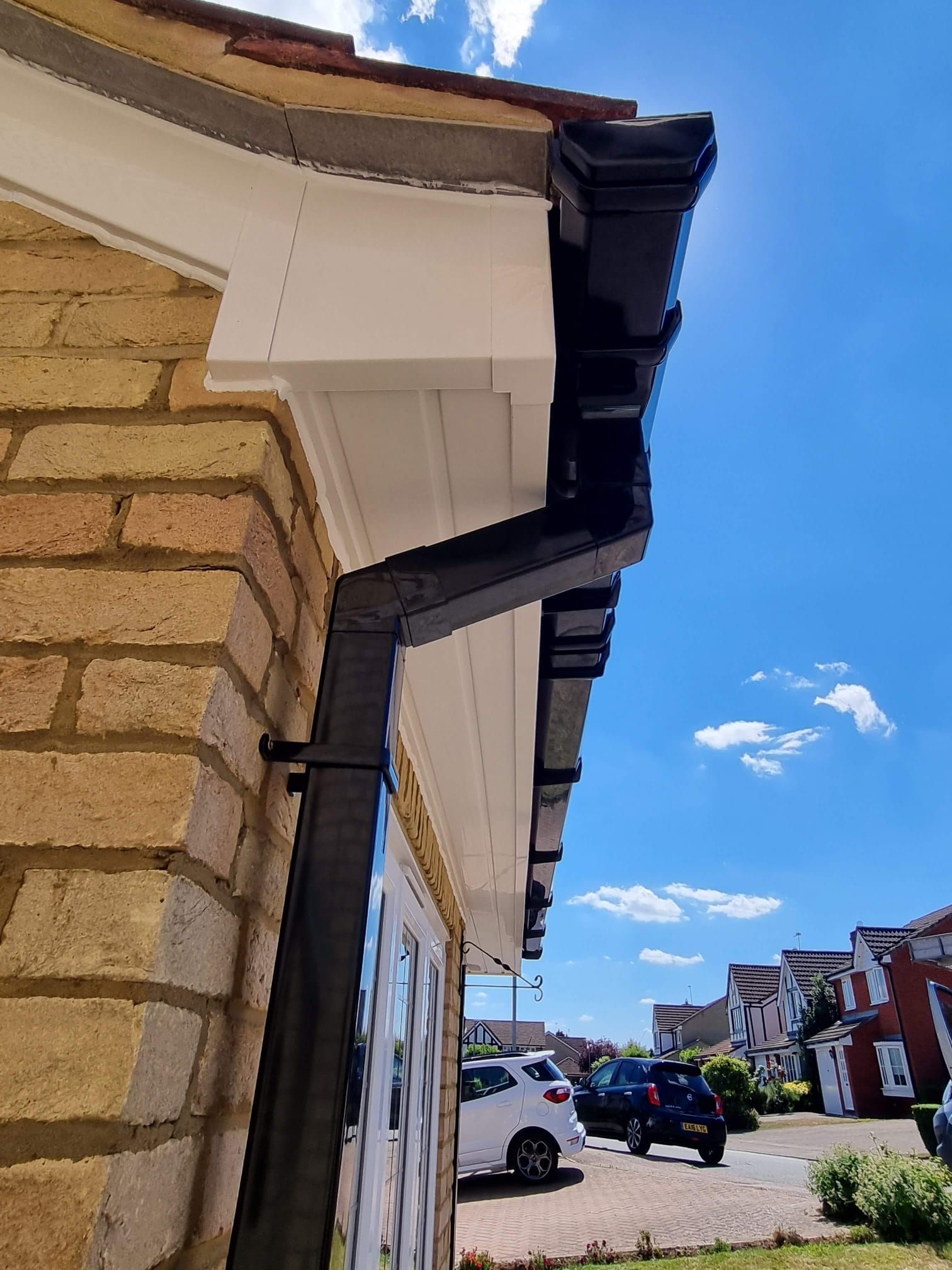 Black gutters and white soffit on a brick building under a blue sky.