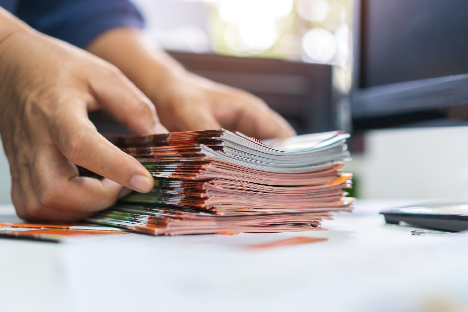 Hands organize a stack of freshly printed marketing cards on a worktable.