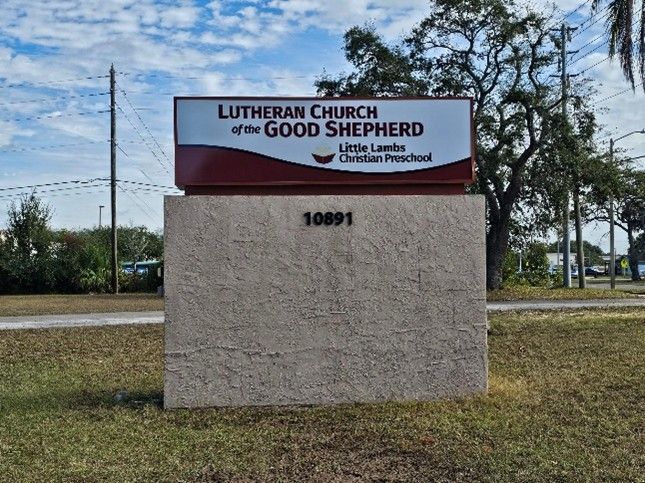 Custom outdoor school sign displayed on a brick base near a church and preschool entrance.