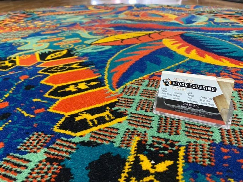 Close-up of a colorful patterned carpet with a sample card on it. The carpet has blue, orange, yellow, and green tones — Mareeba Floor Covering Centre in Mareeba, QLD