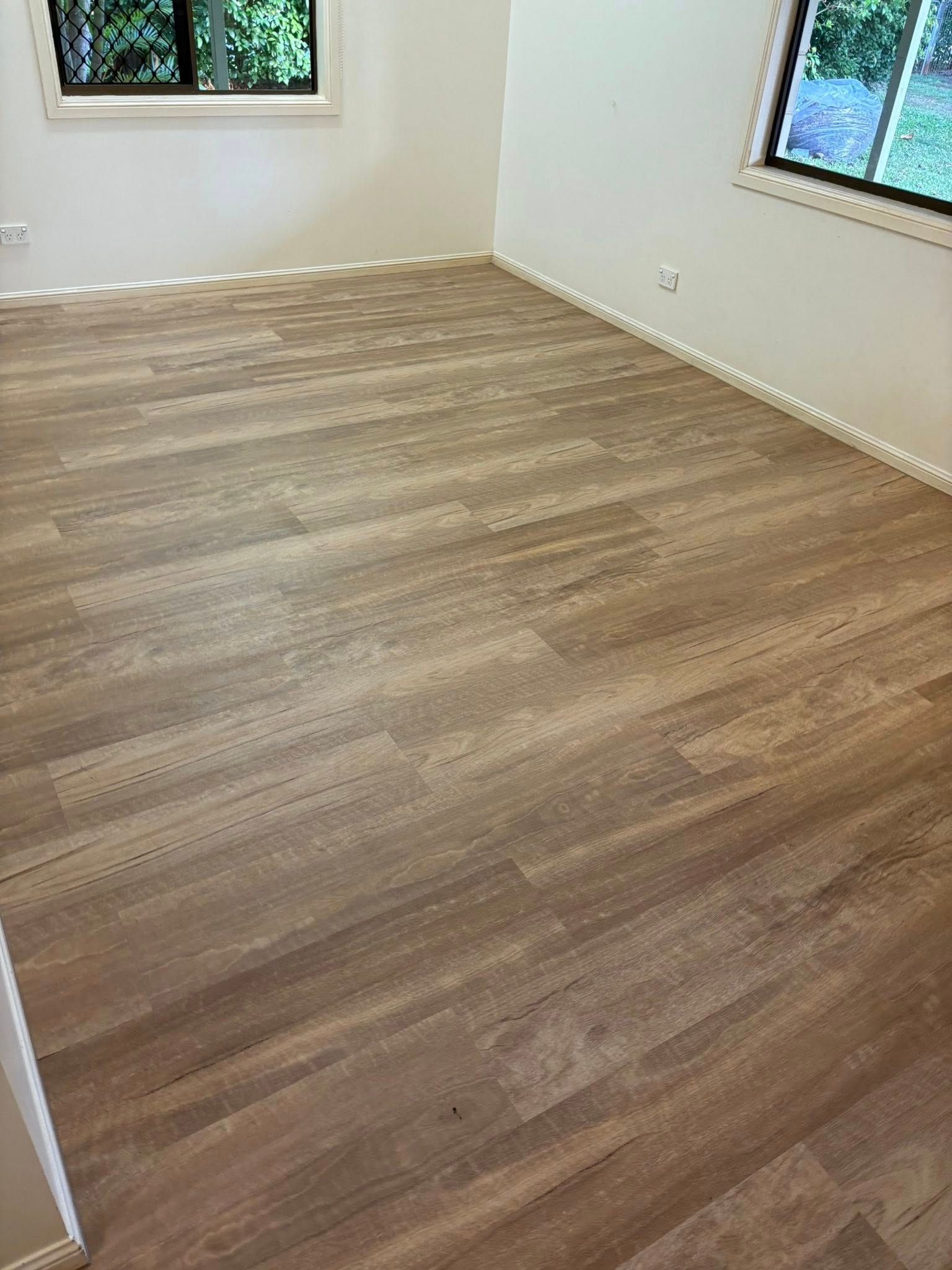 Empty room with light brown wood-look flooring, white walls, and two windows — Mareeba Floor Covering Centre in Mareeba, QLD