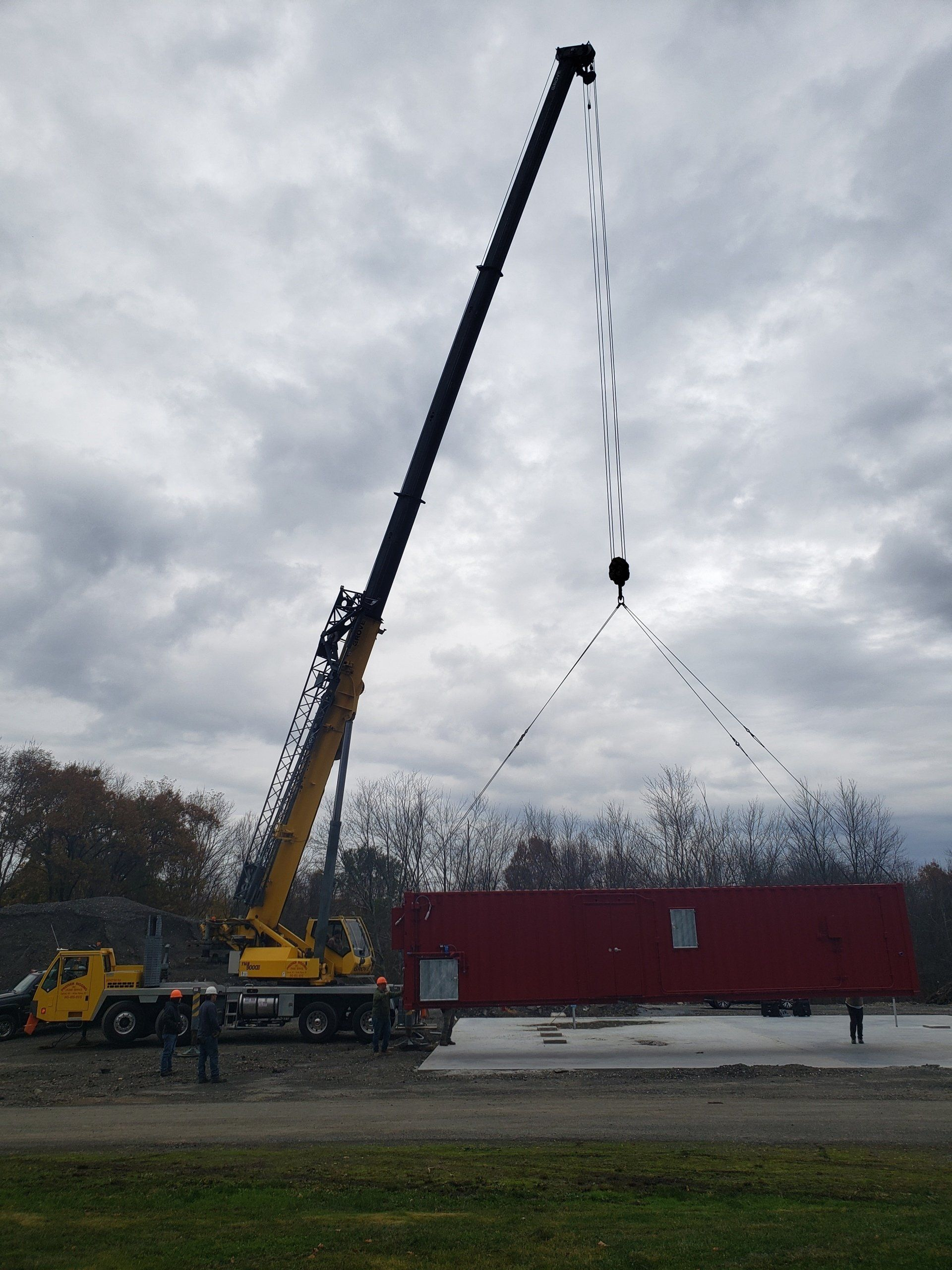 A large yellow crane is lifting a red box