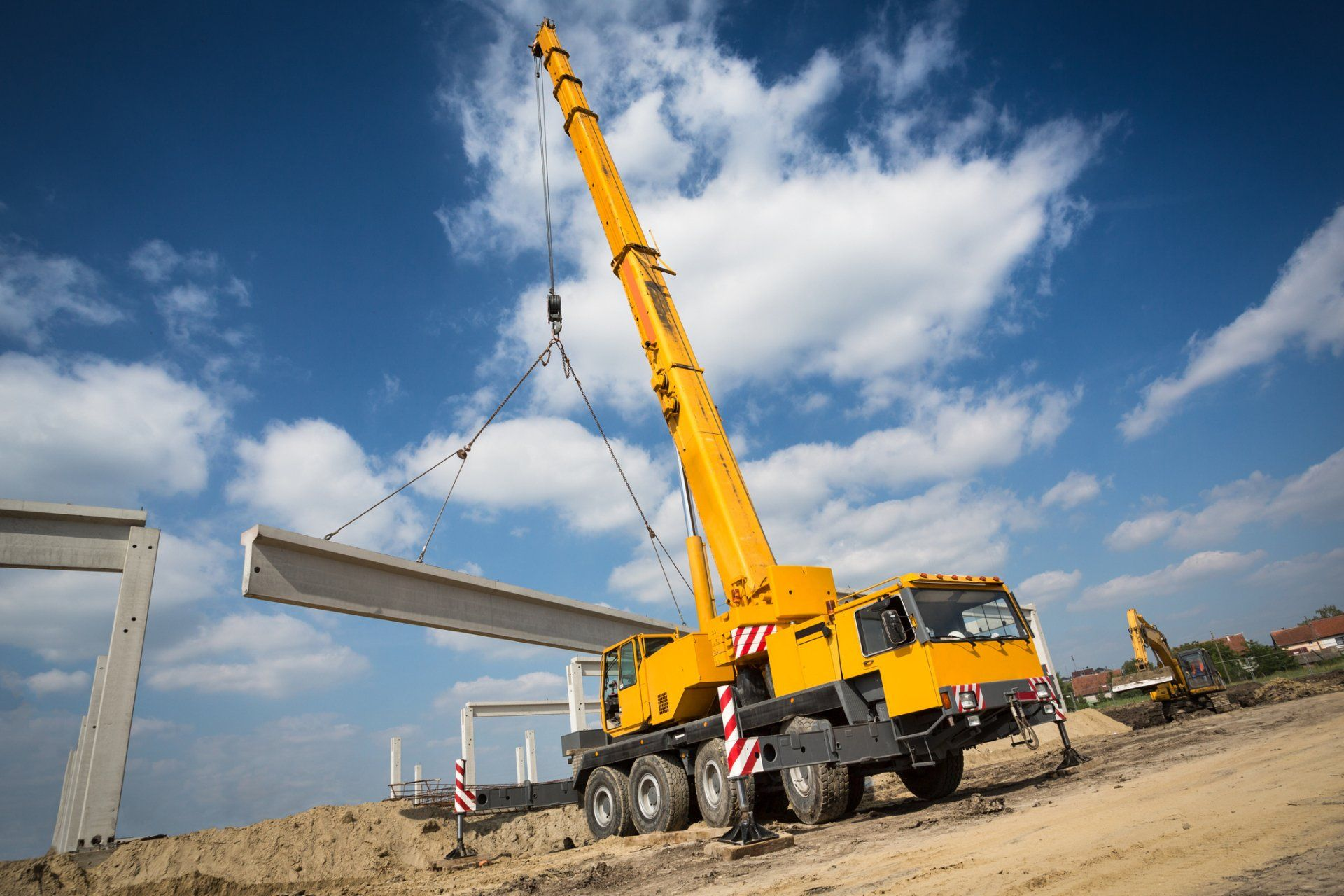 A yellow crane is lifting a concrete beam on a construction site.