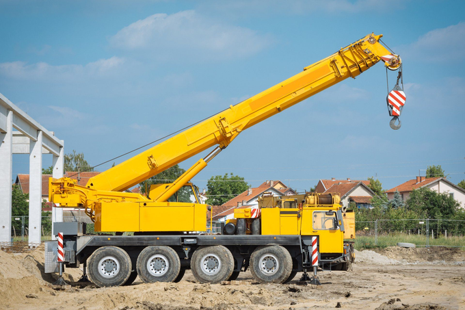 A yellow crane is parked in a dirt field at a construction site.