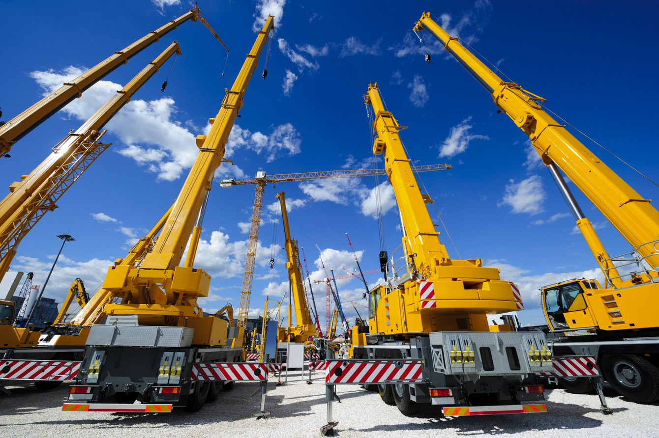 A row of yellow construction cranes are parked in a parking lot.