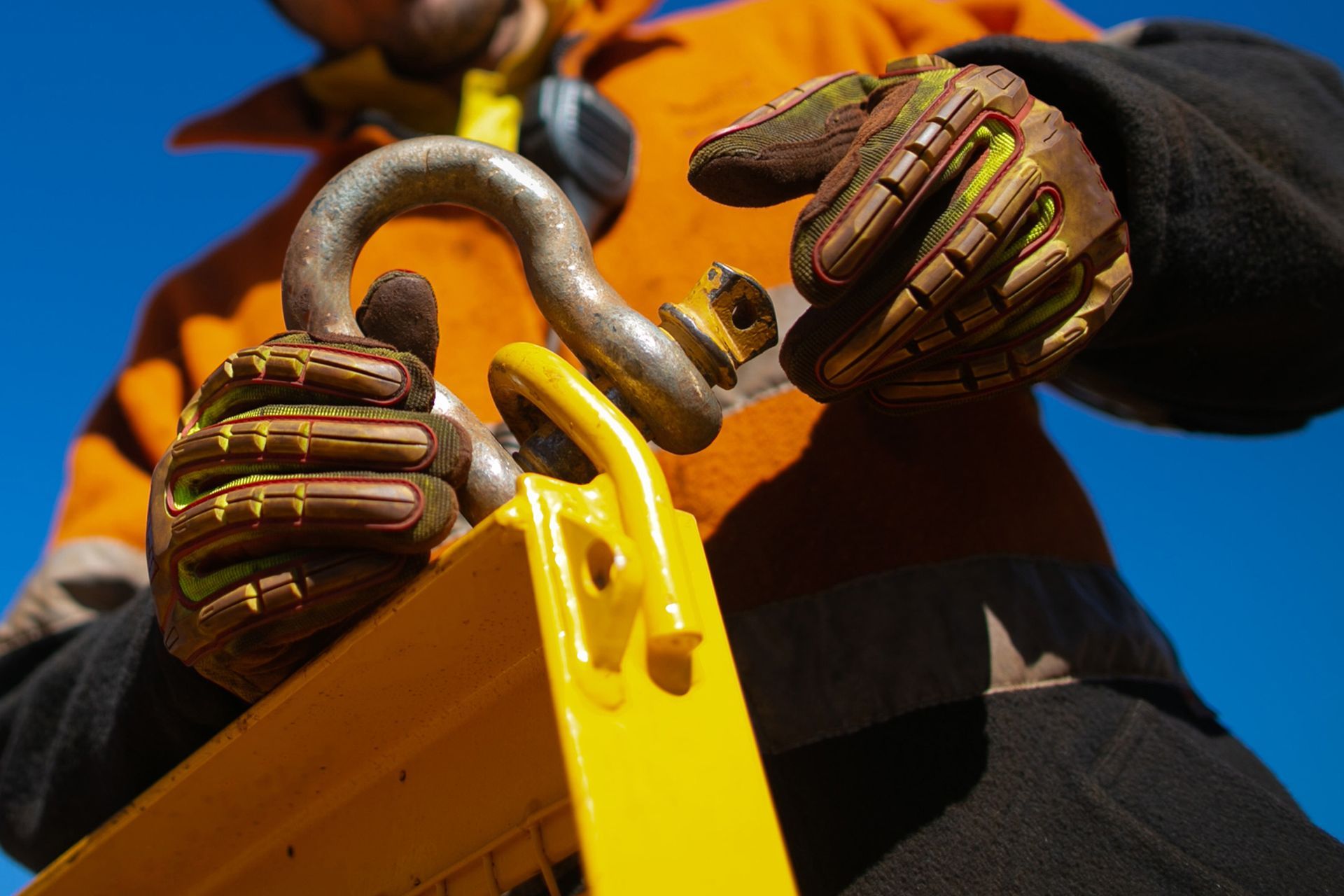 A man wearing gloves is holding a hook on a yellow object.