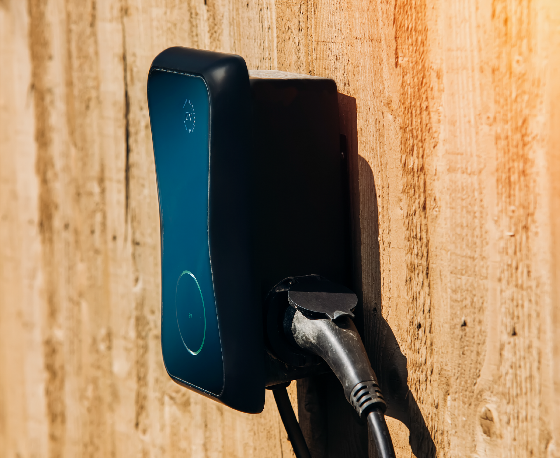 A black electric car charger is attached to a wooden wall.