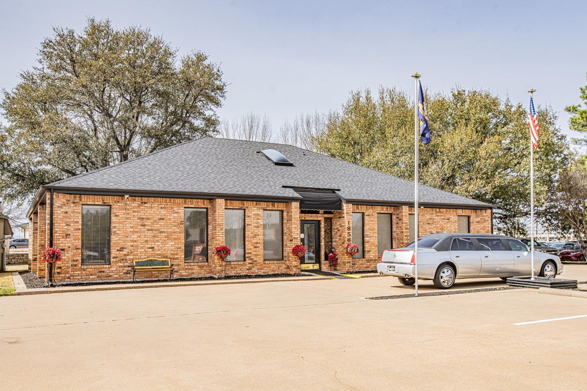 Brick building with dark roof, windows, and flags. A limousine is parked in front.