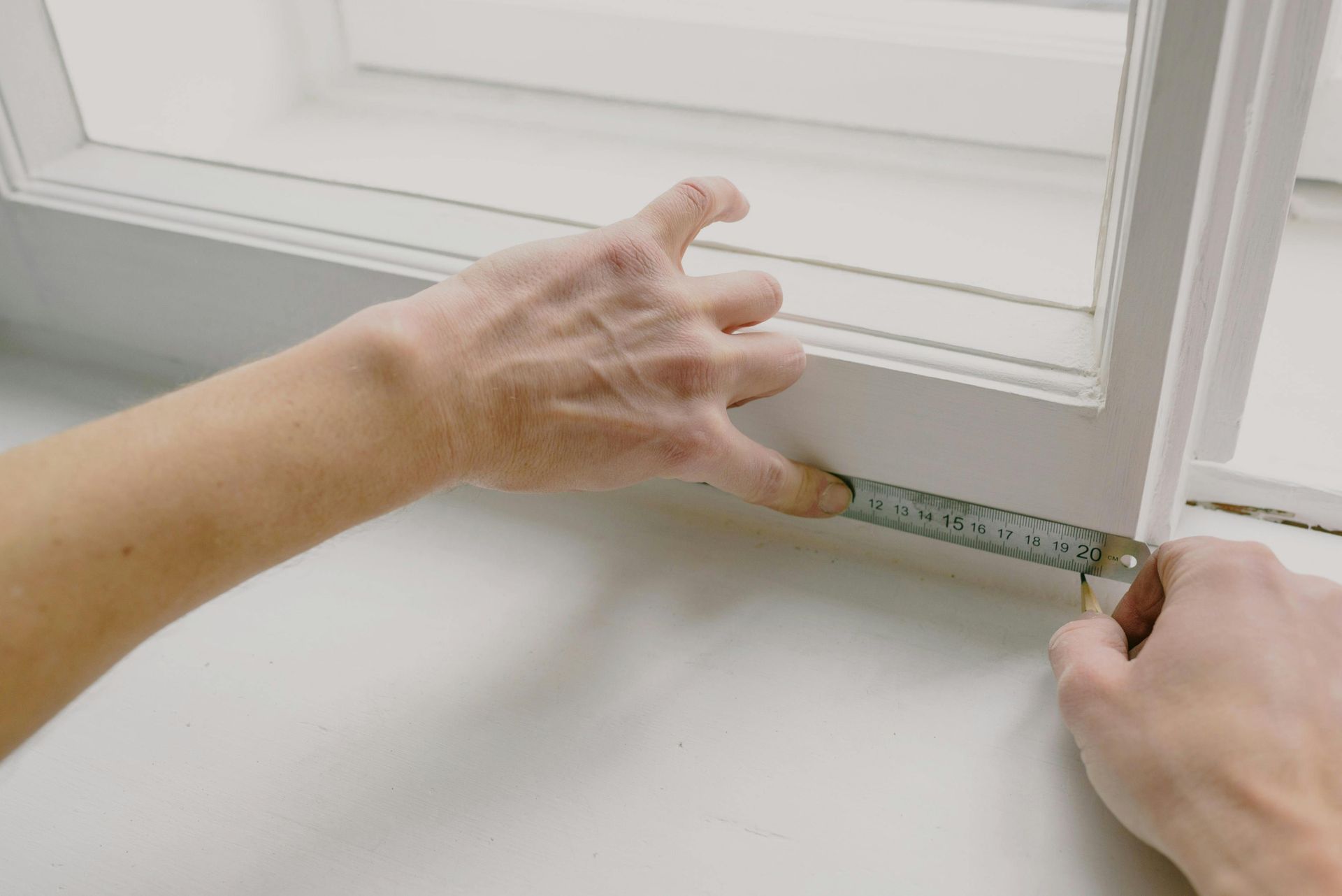 Hands measure the width of a window frame with a ruler. White window frame and sill.