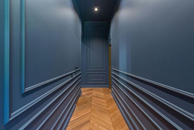Narrow hallway with dark blue walls, decorative trim, and herringbone wood floor.