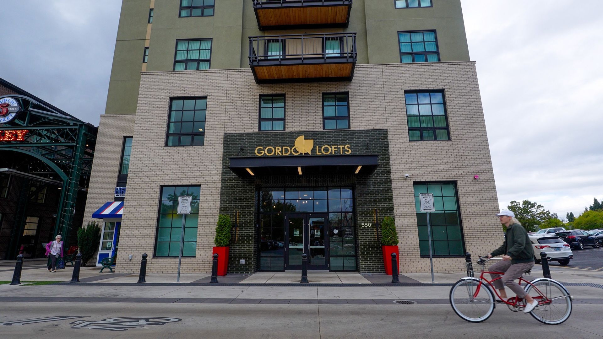A cyclist passes the entrance of Gordon Lofts in downtown Eugene’s 5th Street Public Market District, highlighting walkable streets and car-light, bike-friendly apartment living.