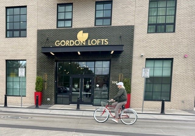 The exterior of Gordon Lofts in Eugene’s 5th Street Public Market District as a cyclist passes by, highlighting the walkable, connected neighborhood that naturally becomes part of daily life.