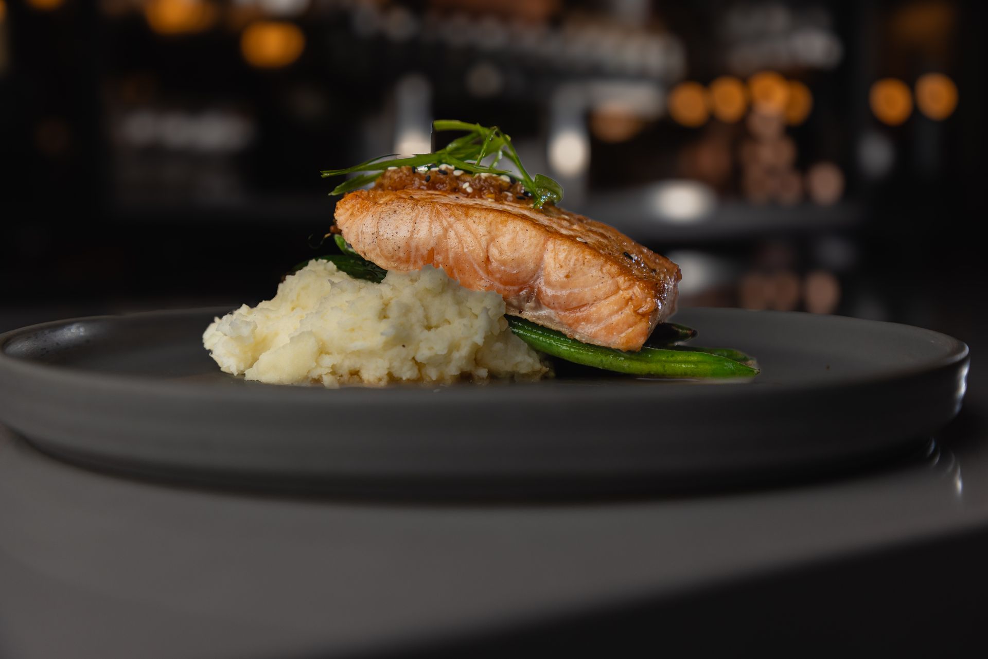 A beautifully plated salmon fillet with crispy skin rests over a bed of creamy mashed potatoes and green beans at Gordon Tavern inside the 5th Street Public Market. The dish glows warmly against a softly lit background, embodying the cozy, seasonal dining experience that makes autumn in Eugene so inviting.