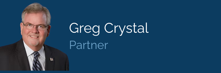A man in a suit and tie is standing in front of a blue background that says greg crystal partner