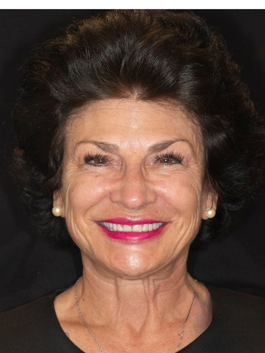 A person with dark hair and a bright smile posing against a dark background.