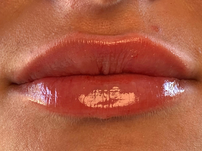 Close-up of lips with a glossy, coral-toned lipstick applied.
