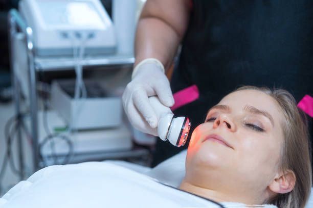 Woman receiving a facial treatment with a red light device.