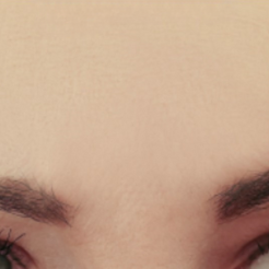 A close-up view of a person's forehead and eyebrows, showing smooth skin and groomed dark eyebrows.
