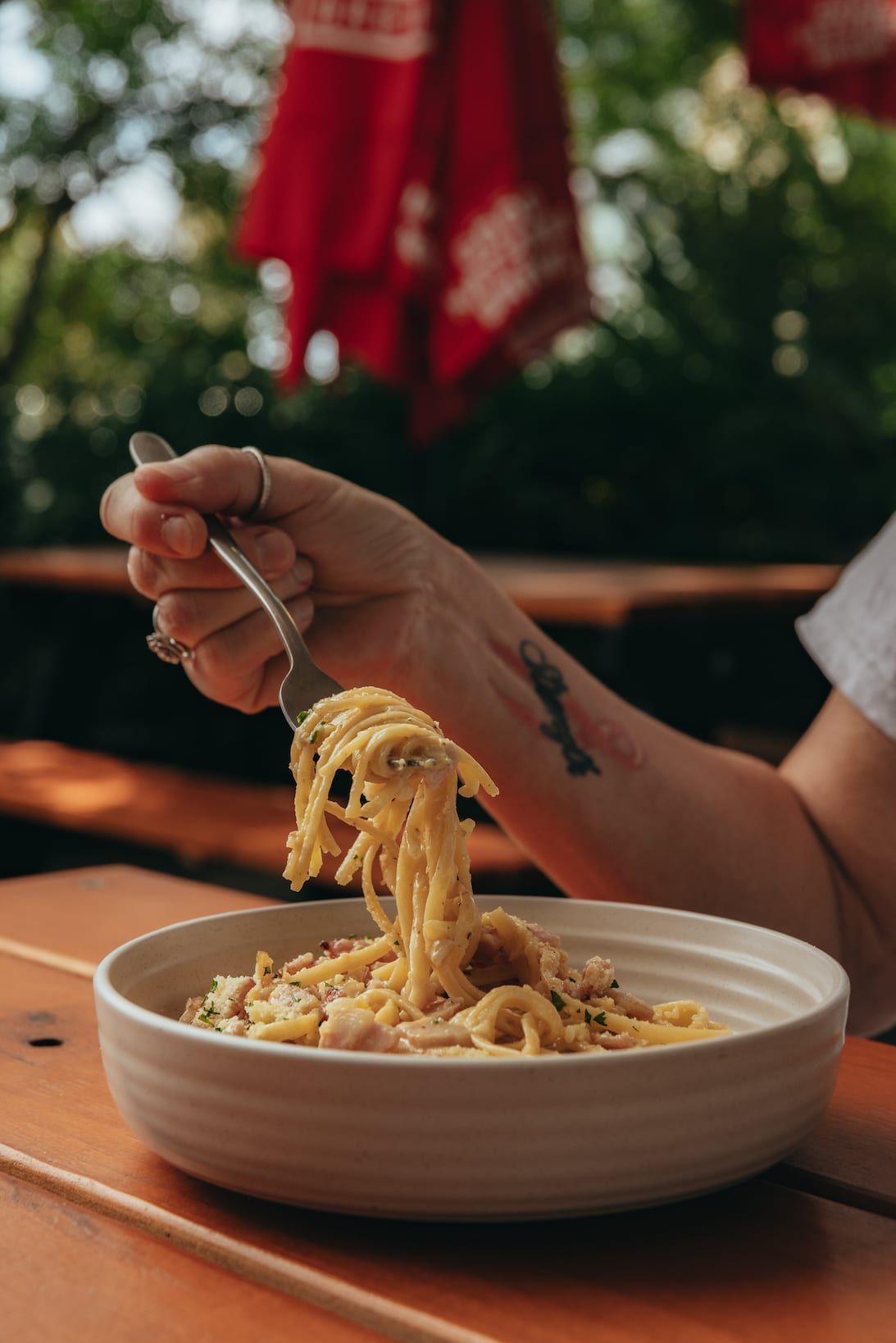 Person eating spaghetti carbonara outside.