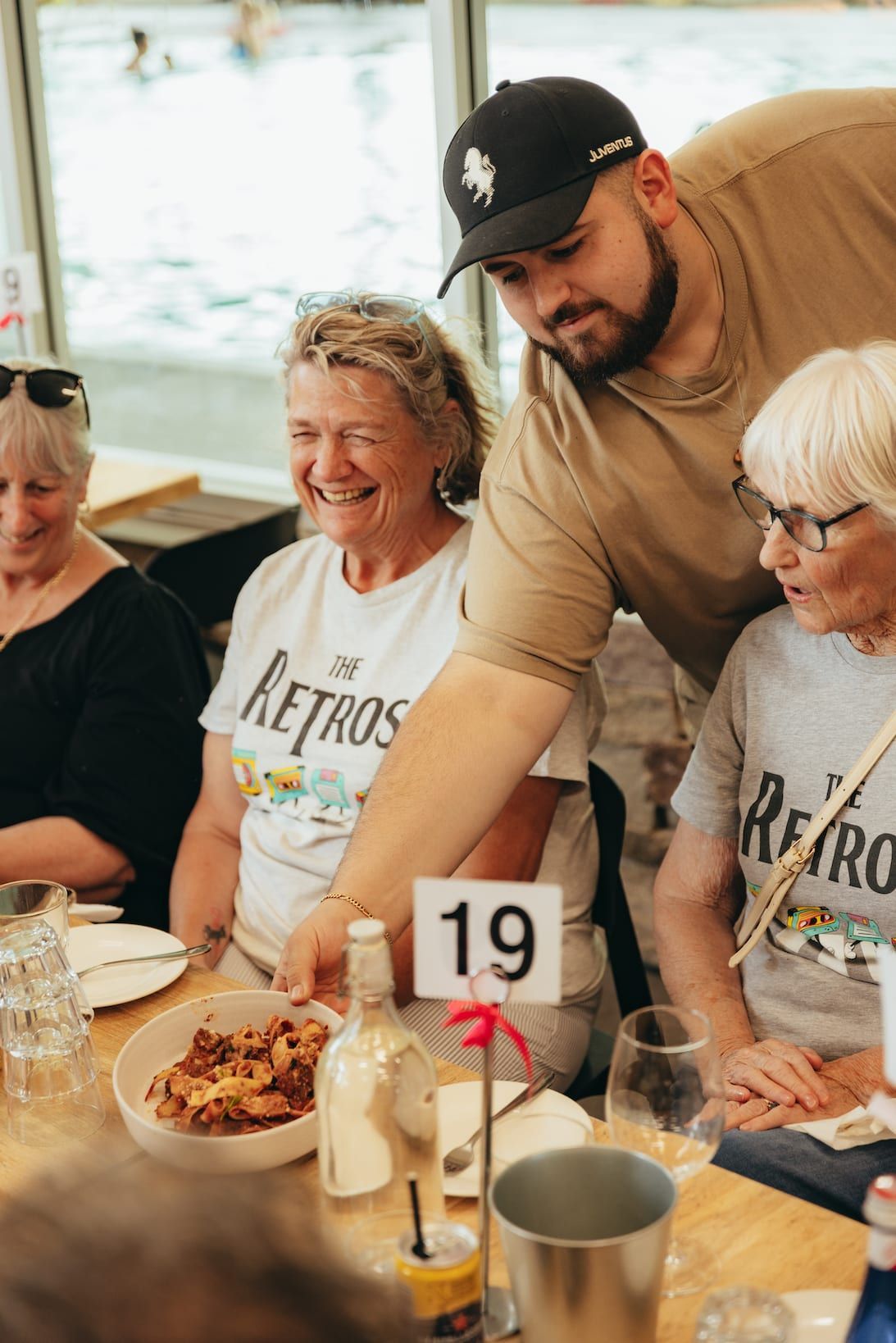 Man serving food to women at a table, wearing matching
