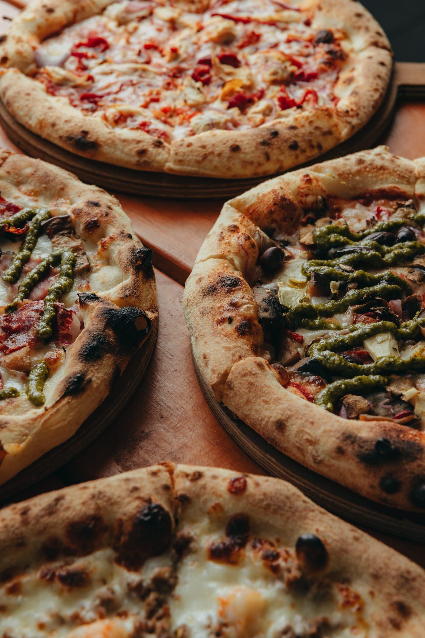 A wooden table topped with a variety of pizzas and french fries.