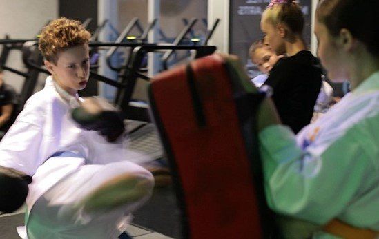 Young boy kicks with right foot while a girl holds the bag