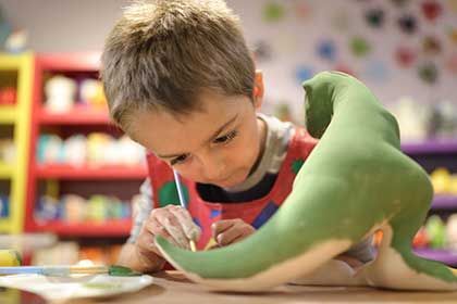 Un niño está pintando un dinosaurio de peluche con un pincel.