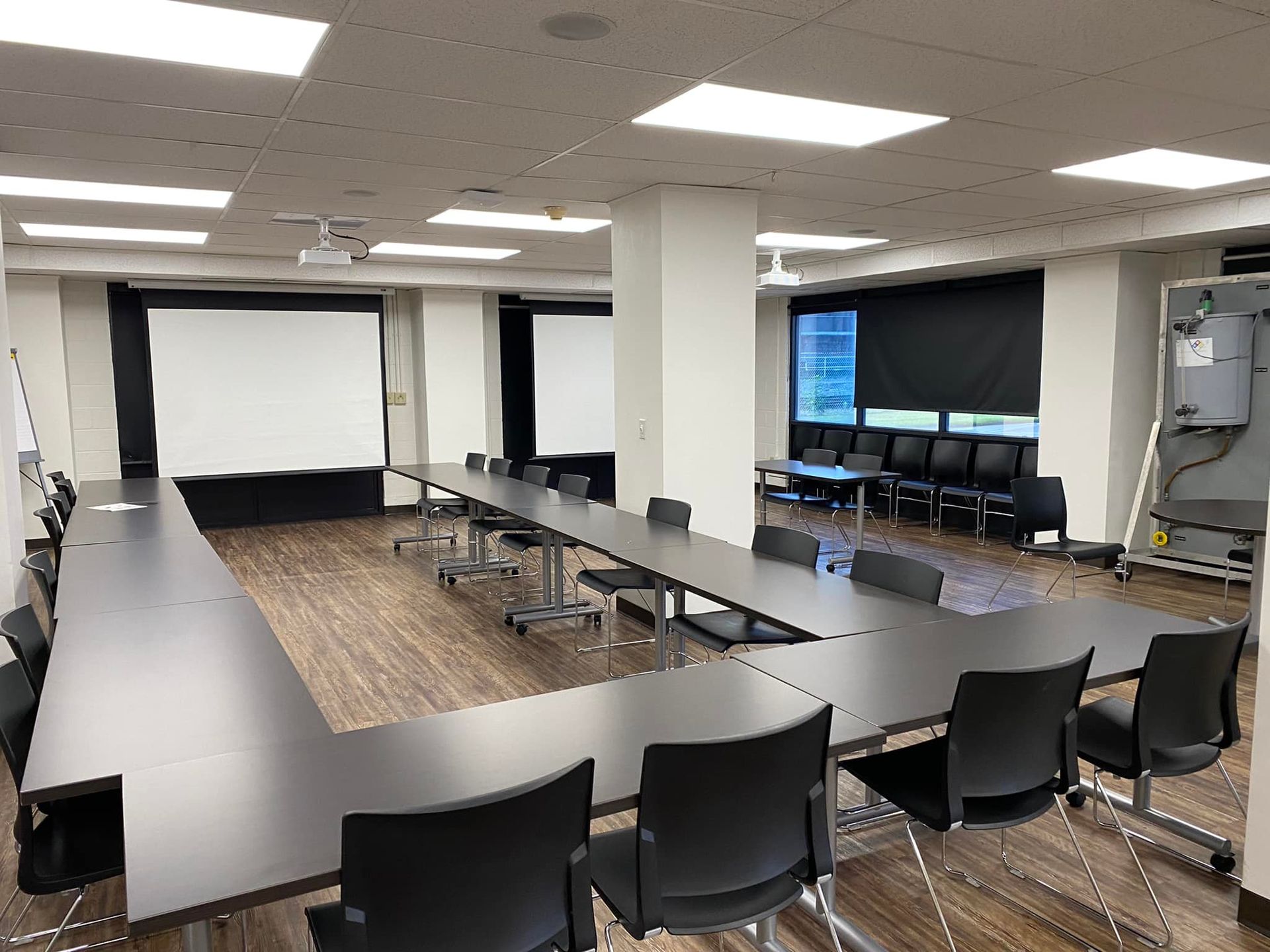 A large conference room with tables and chairs and a large screen.