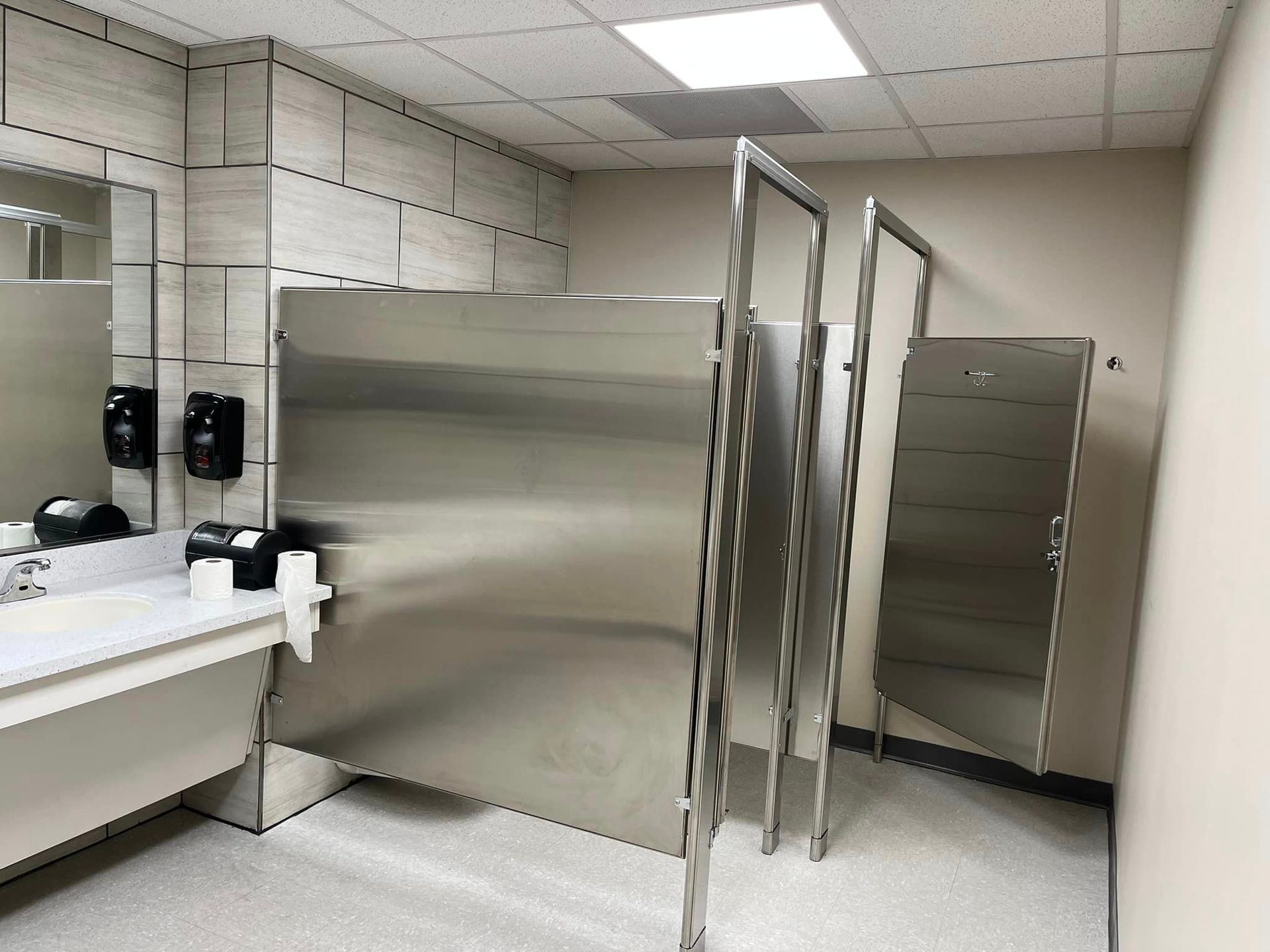 A bathroom with stainless steel stalls and a sink